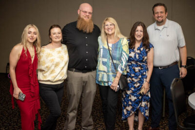 A diverse group of professionals smiling and posing together for a photo at a prom event.